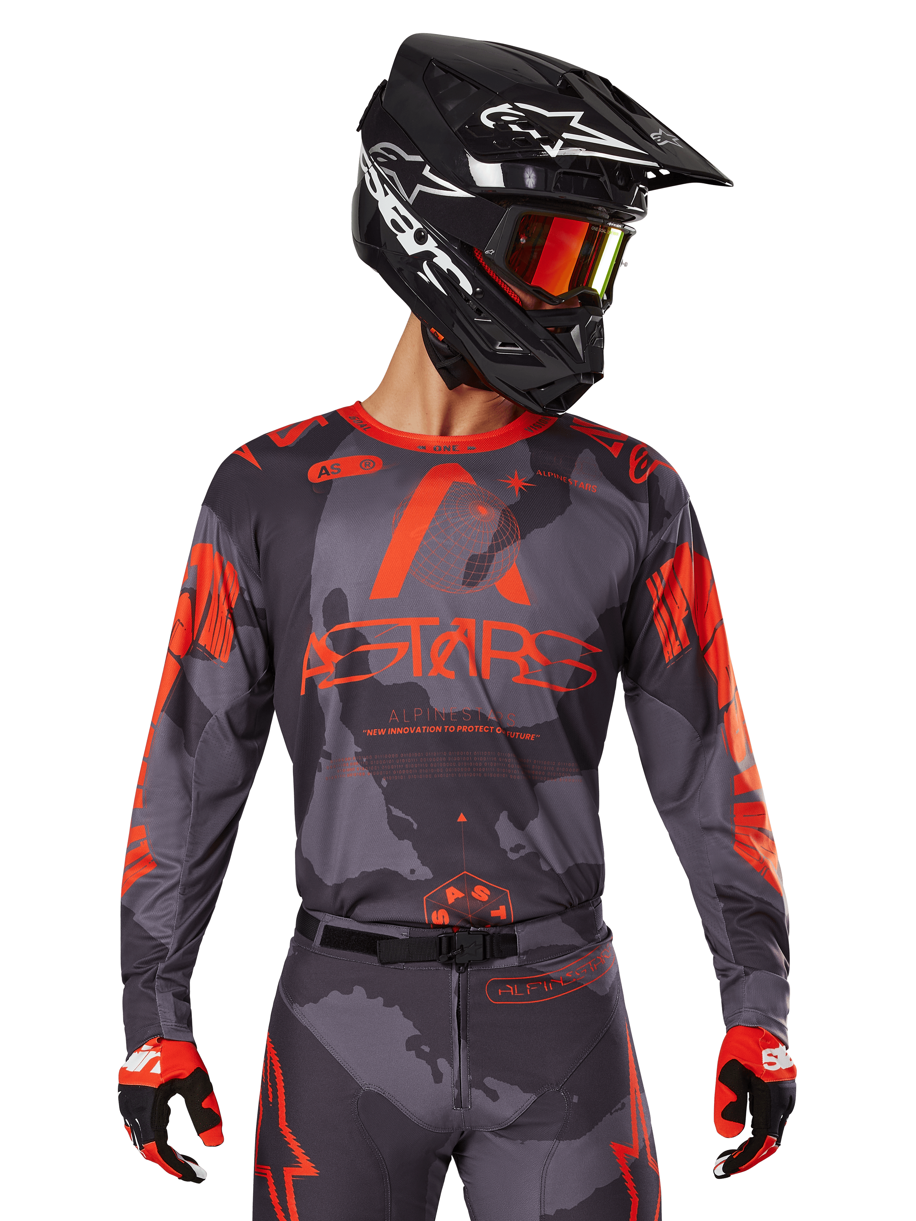 Alpinestars 2025 Racer Hollow Jersey, camisola de motocross, camuflado cinzento e laranja fluorescente, usada com conjunto de equipamento a condizer incluindo calças e luvas, com capacete preto com gráficos brancos e óculos, marca ASTARS em destaque, vestuário desportivo de proteção para motocross