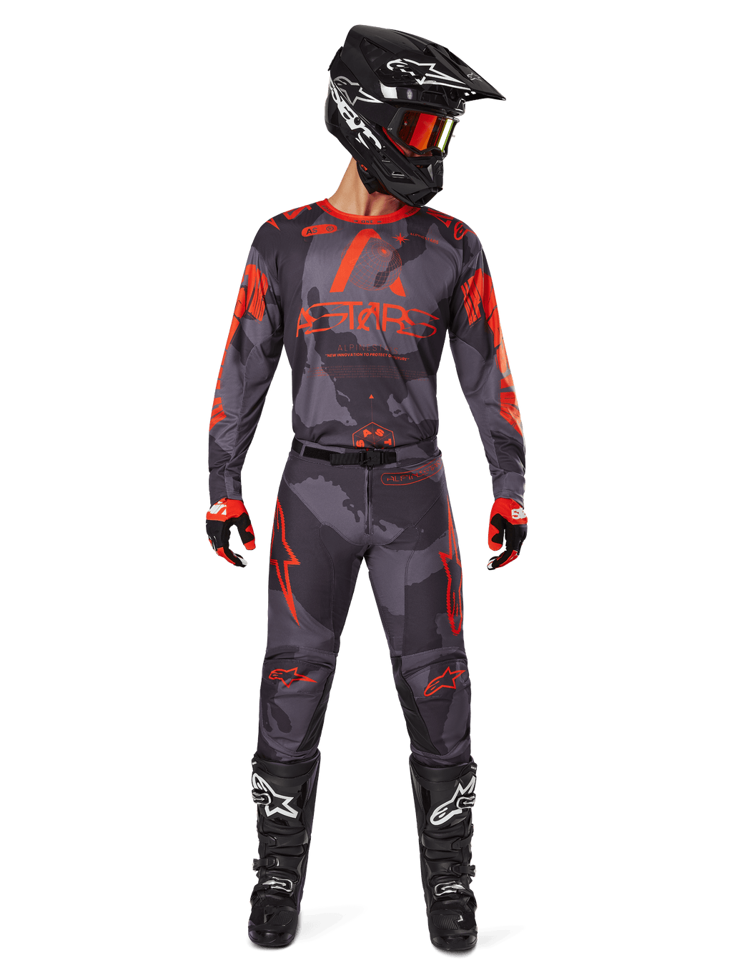 Piloto de motocross com camisola Alpinestars 2025 Racer Hollow e calças a condizer em Camo Cinzento e Laranja Fluo, conjunto completo de equipamento com capacete preto, óculos, luvas e botas, com logótipos laranja vibrantes e padrão de camuflagem.