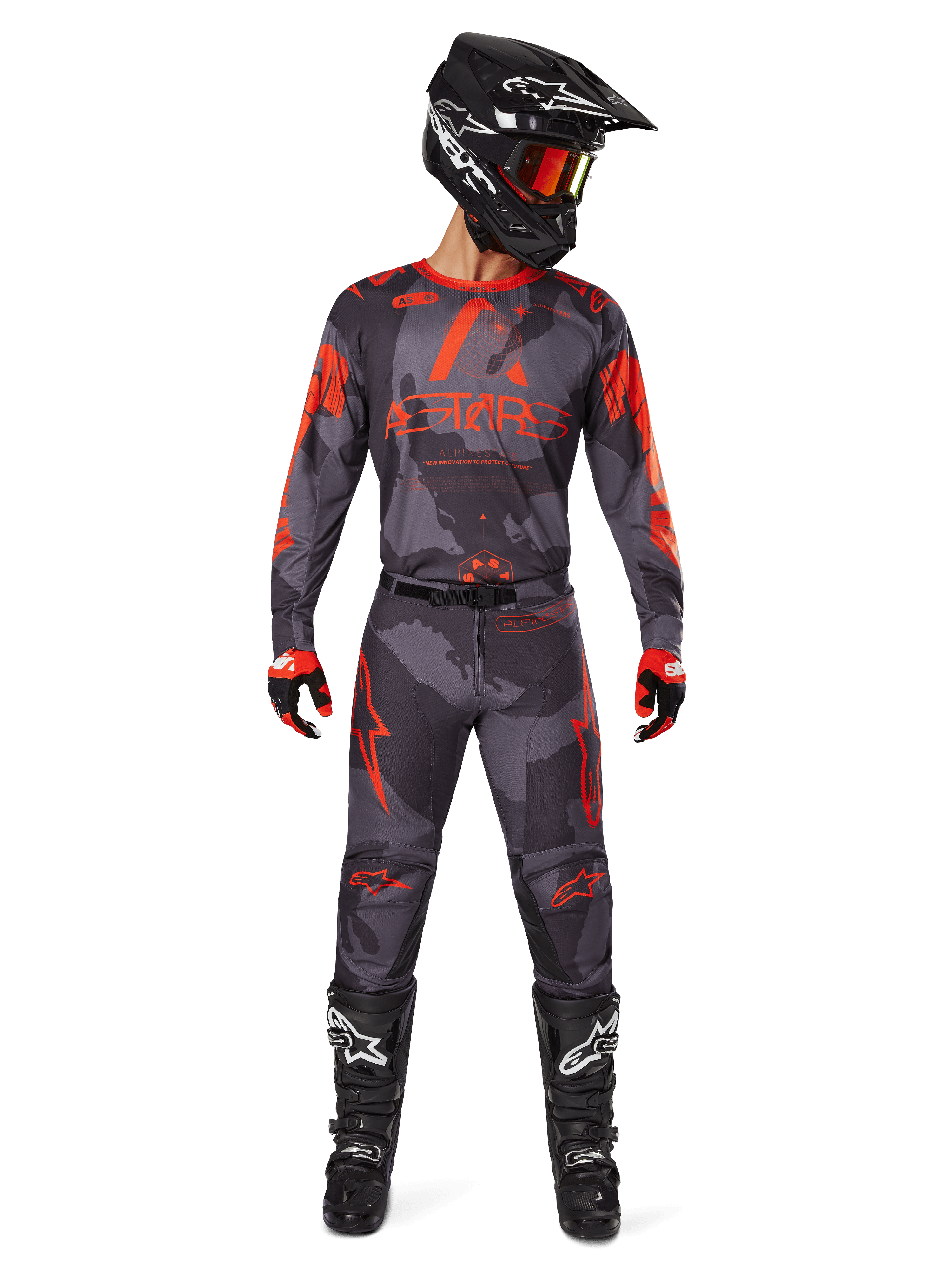 Piloto de motocross com camisola Alpinestars 2025 Racer Hollow e calças a condizer em Camo Cinzento e Laranja Fluo, conjunto completo de equipamento com capacete preto, óculos, luvas e botas, com logótipos laranja vibrantes e padrão de camuflagem.