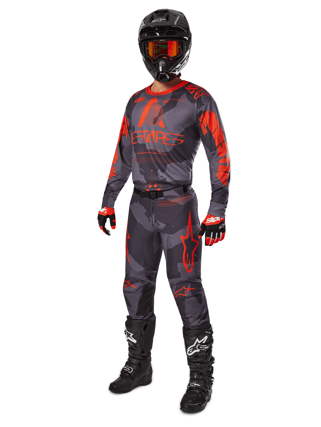 Piloto de motocross com equipamento de corrida completo, camisola e calças Alpinestars 2025 Racer Hollow em Cinzento Camuflado Laranja Fluo, capacete preto com óculos cor de laranja, luvas pretas e vermelhas, e botas pretas com logótipos brancos, conjunto de performance coordenado para corridas todo-o-terreno