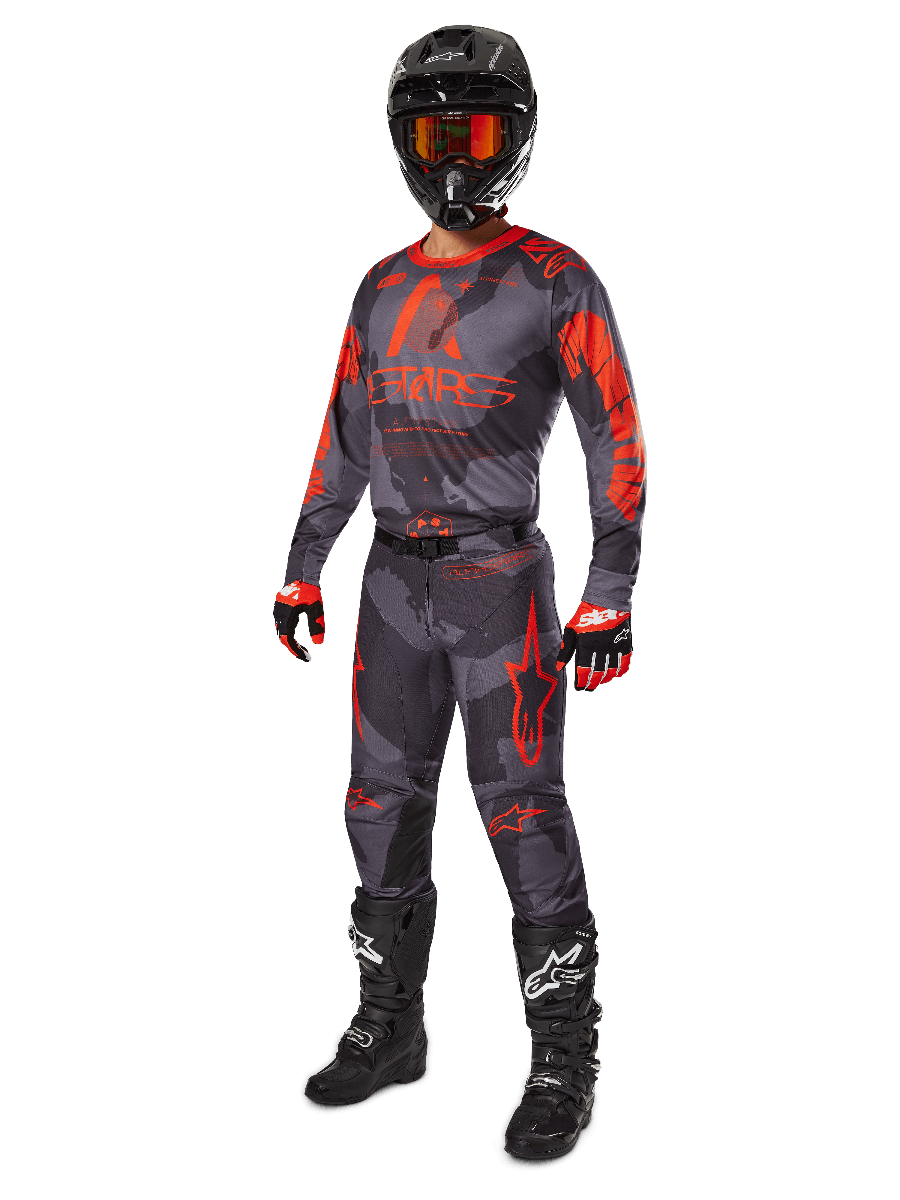 Piloto de motocross com equipamento de corrida completo, camisola e calças Alpinestars 2025 Racer Hollow em Cinzento Camuflado Laranja Fluo, capacete preto com óculos cor de laranja, luvas pretas e vermelhas, e botas pretas com logótipos brancos, conjunto de performance coordenado para corridas todo-o-terreno
