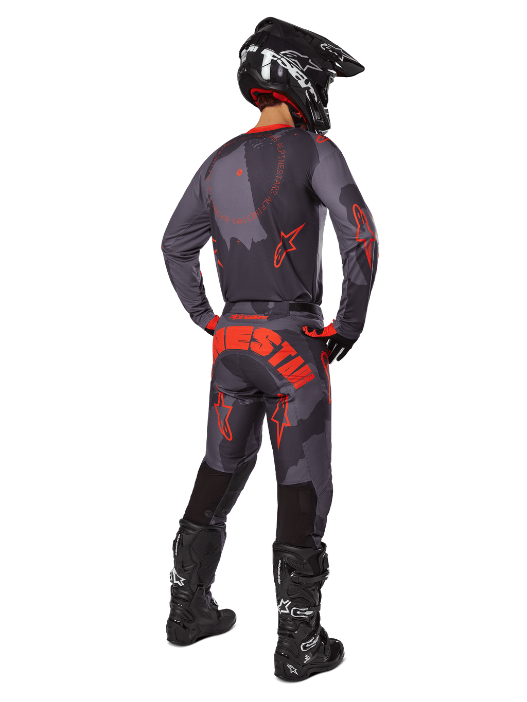 Piloto de motocross visto de trás, a usar a camisola Alpinestars 2025 Racer Hollow em Gray Camo Orange Fluo, calças camufladas a condizer com o texto Alpinestars em cor-de-laranja, capacete preto e botas pretas, conjunto de equipamento coordenado para condução todo-o-terreno