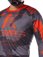 Alpinestars 2025 Racer Hollow Jersey, camisola de motocross, camuflado cinzento e laranja fluo, com logótipo Alpinestars grande em laranja e grafismos técnicos, gola redonda, concebida para condução off-road de alto desempenho