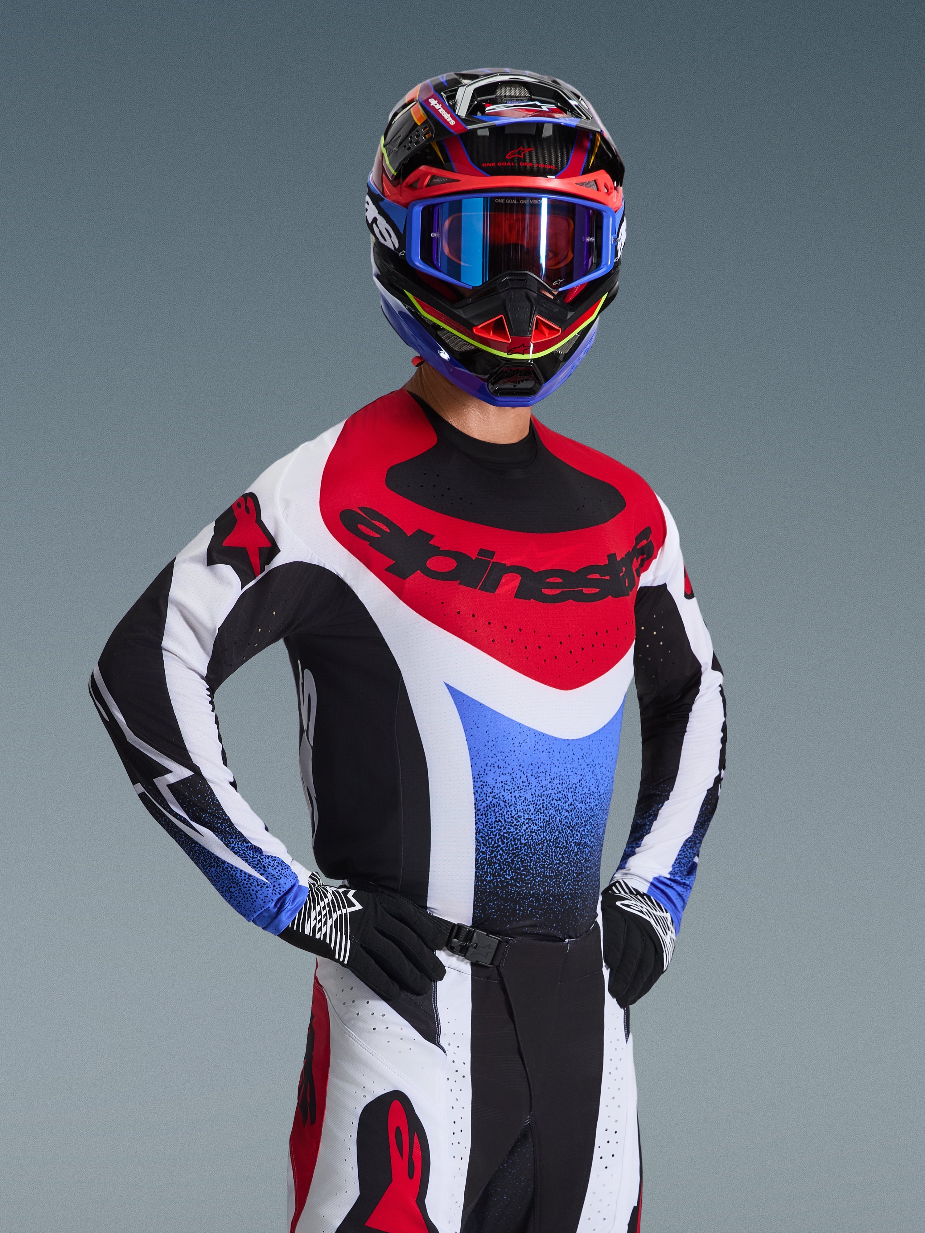 Alpinestars Conjunto de Equipamento Techstar Knif 2026, piloto de motocross com camisola de corrida vermelha, branca e azul com detalhes pretos, capacete e óculos multicoloridos a condizer, luvas pretas, equipamento profissional para competição de motocross.