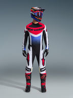 Piloto de motocross a usar o conjunto de equipamento Alpinestars Techstar Knif 2026, camisola preta, branca e vermelha com gradiente azul e logótipos, calças pretas e brancas a condizer com detalhes vermelhos, capacete multicolorido com óculos azuis e botas pretas e vermelhas, fato de corrida todo-o-terreno coordenado.