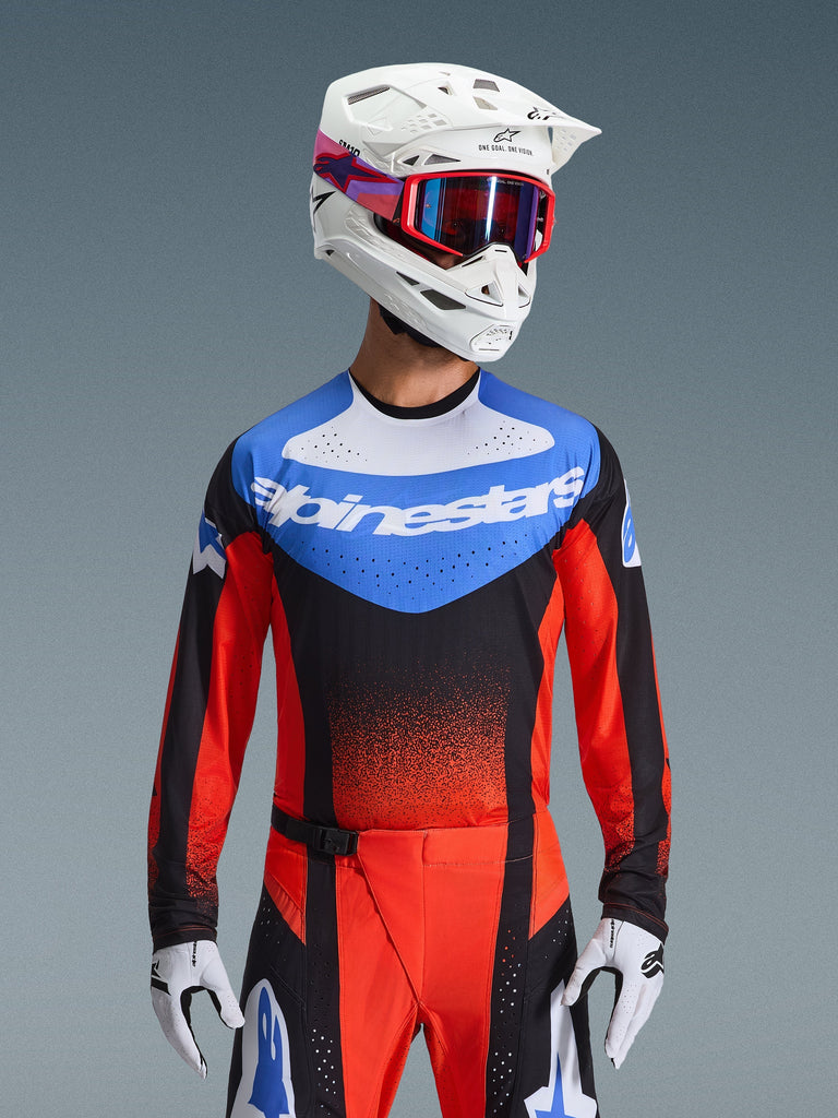 Alpinestars 2026 Techstar Knif Jersey, Motocross Jersey, Orange Black and UCLA Blue, featuring a blue chest panel with white Alpinestars logo and orange-red sleeves, worn with a white helmet, red goggles, and white gloves, professional off-road racing gear