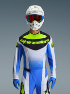 Alpinestars 2026 Techstar Knif Gear Set, piloto de motocross com equipamento de corrida azul, branco e amarelo néon, camisola com painel frontal preto e logótipo amarelo néon, capacete branco com óculos coloridos, luvas e calças azuis a condizer, fato de corrida atlético de alta performance para competição todo-o-terreno