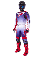 Piloto de motocross a usar o Conjunto de Equipamento Alpinestars 2025 Fluid Wurx, camisola roxa e vermelho vivo com detalhes brancos, calças de motocross a condizer, botas vermelho vivo, capacete preto com óculos de proteção azuis, e luvas vermelhas e pretas, equipamento profissional completo para corridas todo-o-terreno