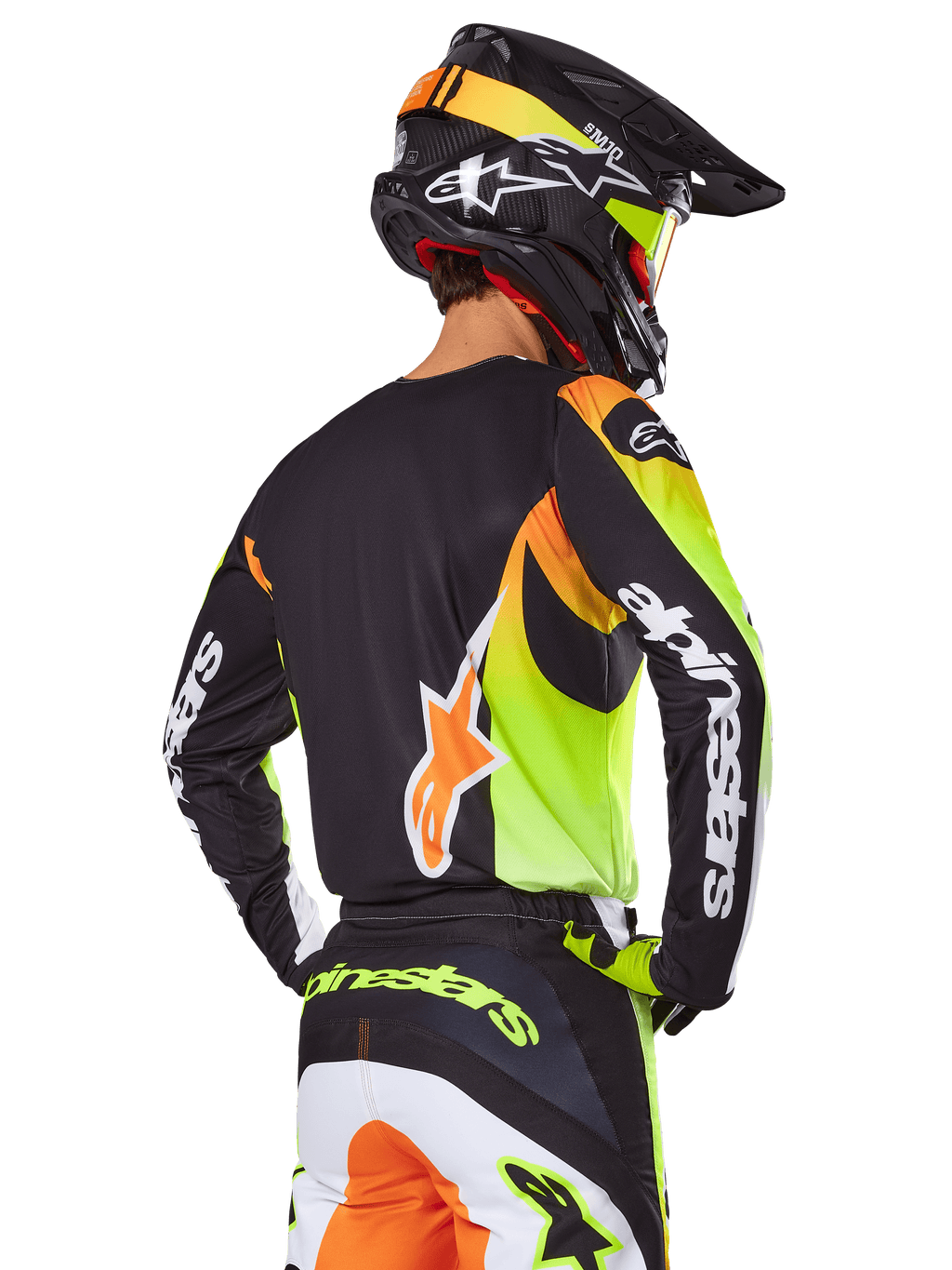 Piloto de motocross visto de costas com o conjunto de equipamento Alpinestars 2025 Fluid Wurx, camisola preta com gráficos vibrantes em amarelo néon e laranja, calças a condizer com painéis brancos e laranja, capacete preto com detalhes néon, logótipo Alpinestars em destaque nas mangas e no assento