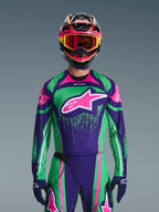 Conjunto de Equipamento Alpinestars 2026 Techstar Nomur, piloto de motocross a usar camisola de corrida em verde vibrante e roxo com detalhes cor-de-rosa, conjunto condizente com capacete e óculos multicoloridos, fato de motociclismo de alta performance para todo-o-terreno