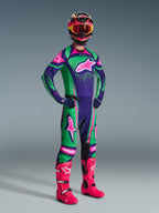Piloto de motocross com o conjunto Alpinestars 2026 Techstar Nomur em roxo escuro, verde e rosa fluo, com camisola e calças a condizer, capacete colorido com óculos cor-de-rosa e botas cor-de-rosa vibrantes, equipamento profissional de competição todo-o-terreno