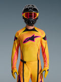 Alpinestars Camisola Techstar Nomur 2026 em laranja, amarelo e rosa, usada por um piloto de motocross com um capacete preto e óculos cor-de-rosa a condizer, com um grande logótipo Alpinestars rosa no peito e um ajuste atlético de corrida para desempenho fora de estrada