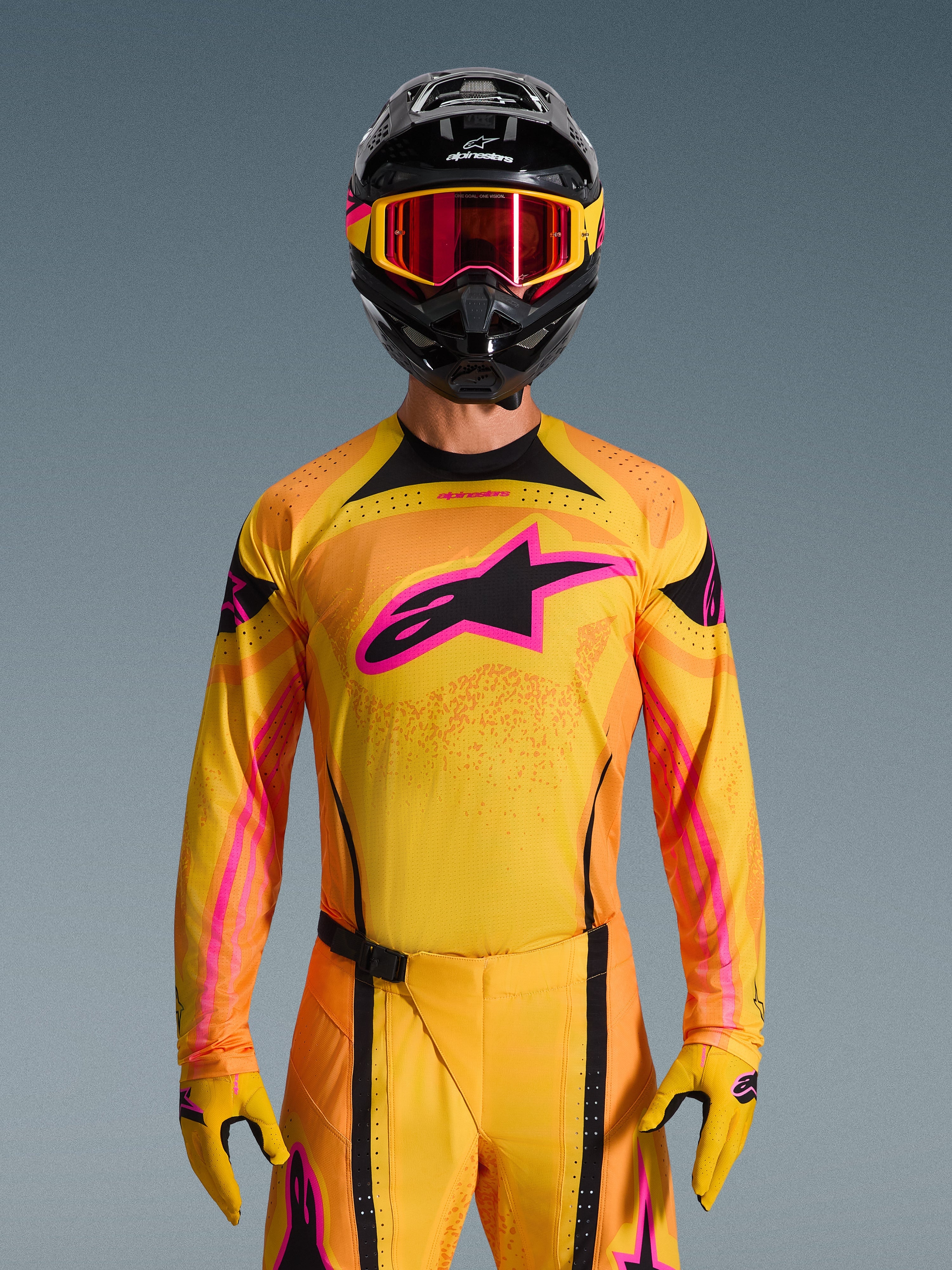 Alpinestars Camisola Techstar Nomur 2026 em laranja, amarelo e rosa, usada por um piloto de motocross com um capacete preto e óculos cor-de-rosa a condizer, com um grande logótipo Alpinestars rosa no peito e um ajuste atlético de corrida para desempenho fora de estrada