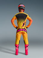 Piloto de motocross visto de costas, a usar a Camisola Alpinestars 2026 Techstar Nomur em Laranja Amarelo Rosa, equipamento de corrida coordenado incluindo calças a condizer com logótipo rosa vibrante e botas rosa choque, corte atlético de corrida para desempenho off-road de nível avançado