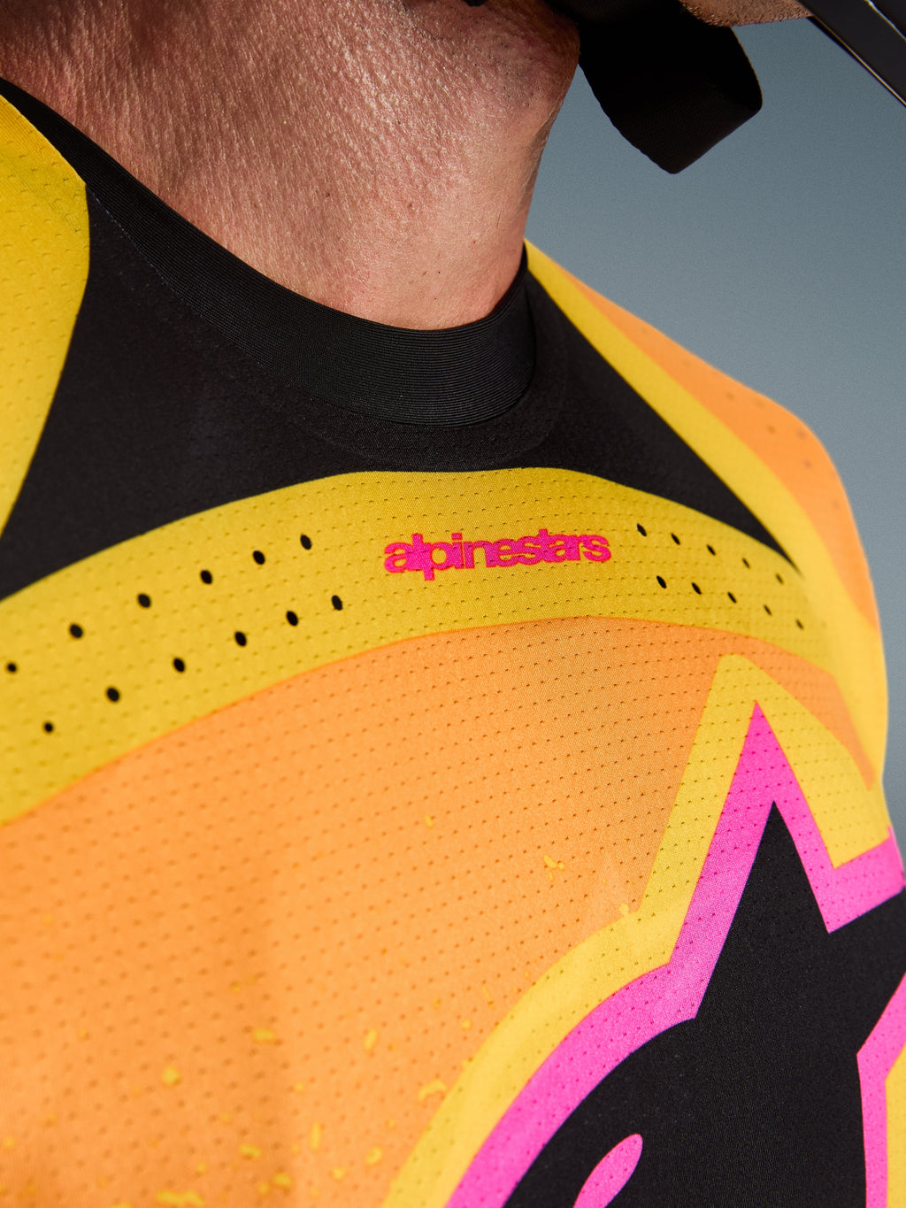 Alpinestars 2026 Techstar Nomur Jersey, camisola de motocross, laranja, amarelo e rosa, pormenor em grande plano do peito e da gola, com ventilação cortada a laser, logótipo cor-de-rosa e tecido de malha respirável