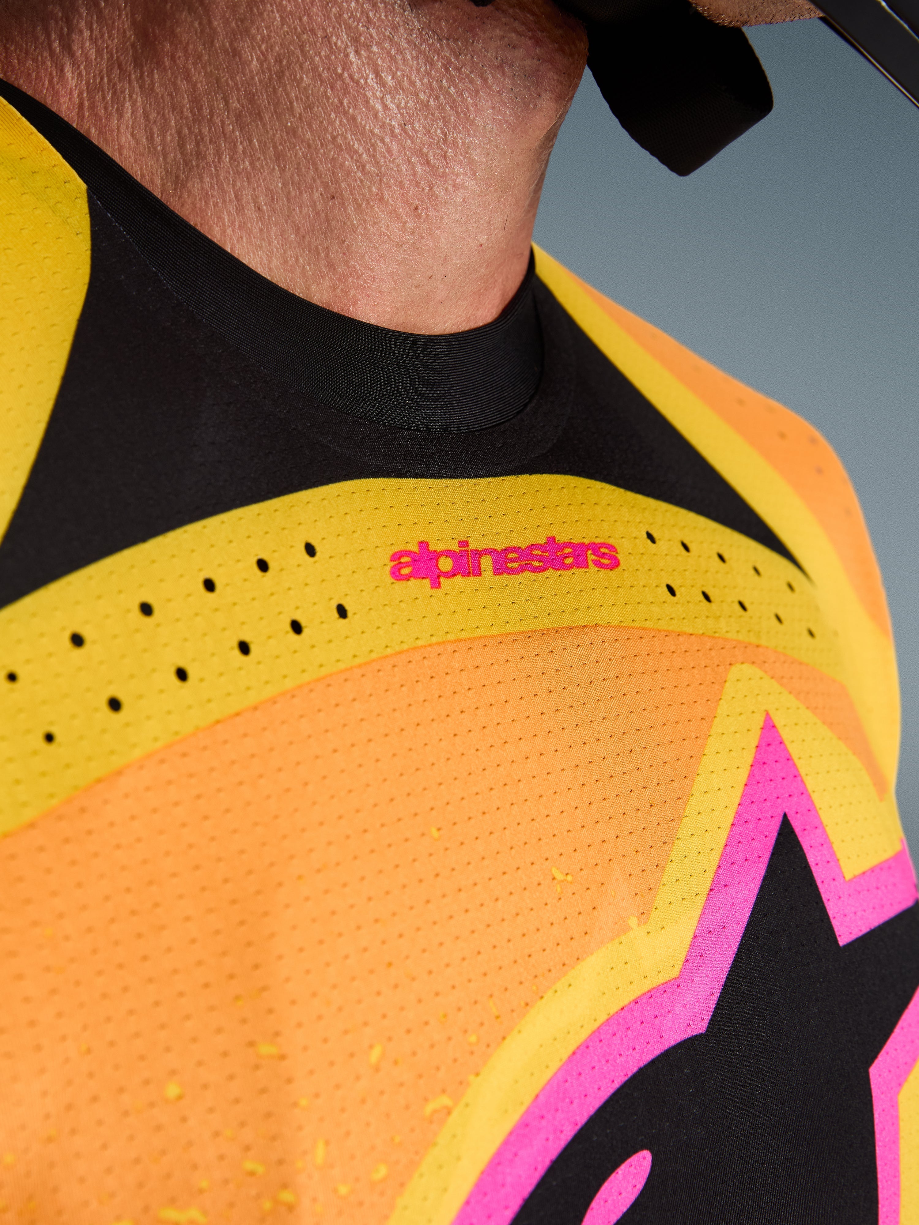 Alpinestars 2026 Techstar Nomur Jersey, camisola de motocross, laranja, amarelo e rosa, pormenor em grande plano do peito e da gola, com ventilação cortada a laser, logótipo cor-de-rosa e tecido de malha respirável