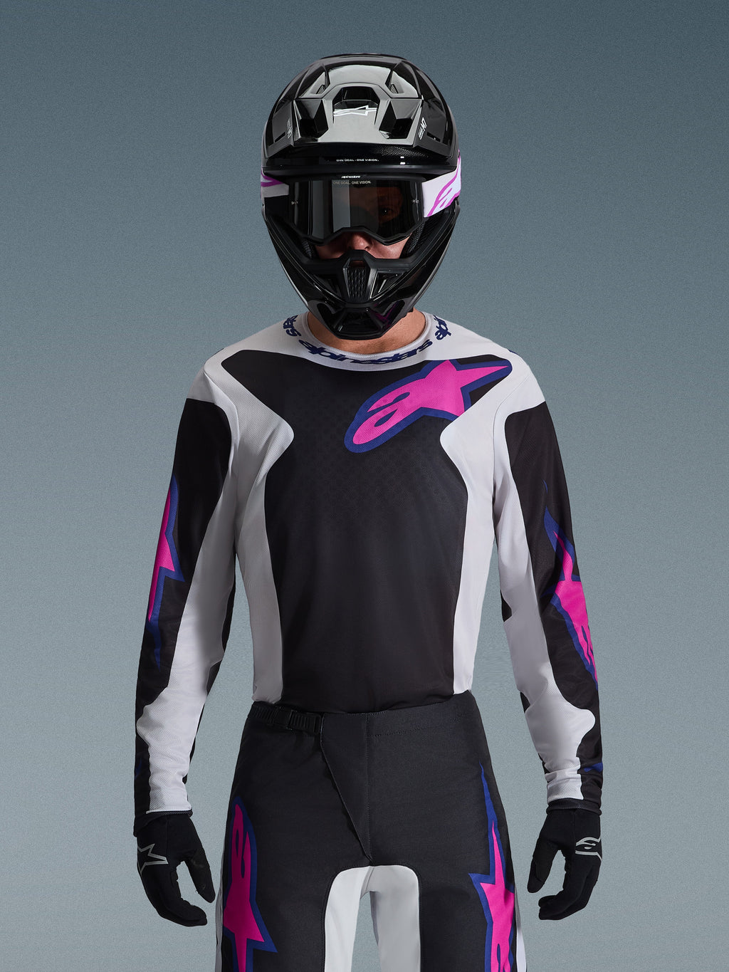 Camisola Alpinestars 2026 Fluid Grid, camisola de motocross, preta, cinzento claro e roxo, usada por um piloto com calças de motocross a condizer, capacete preto e óculos de proteção, conjunto completo de equipamento de corrida de alta performance