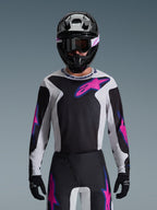 Camisola Alpinestars 2026 Fluid Grid, camisola de motocross, preta, cinzento claro e roxo, usada por um piloto com calças de motocross a condizer, capacete preto e óculos de proteção, conjunto completo de equipamento de corrida de alta performance