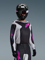 Piloto de motocross com camisola Alpinestars 2026 Fluid Grid em preto, cinzento claro e roxo, com grandes logótipos de estrela rosa e roxo, calças a condizer, capacete preto e óculos de proteção, conjunto completo de equipamento de corrida todo-o-terreno