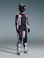 Piloto de motocross com equipamento de competição completo, Camisola Fluid Grid 2026 em preto com detalhes em cinzento claro e roxo, calças Fluid Grid a condizer, capacete preto com óculos coordenados, botas brancas e pretas, e luvas pretas, cenário de estúdio profissional para corridas todo-o-terreno.