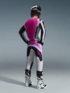 Piloto de motocross visto de costas a usar a camisola Alpinestars Fluid Grid 2026, camisola branca com um grande painel traseiro cor-de-rosa choque e logótipos roxos, calças brancas e pretas a condizer com detalhes cor-de-rosa, botas brancas e capacete preto, equipamento de corrida todo-o-terreno coordenado
