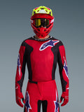 Alpinestars 2026 Fluid Grid Jersey, camisola de motocross, vermelha, preta e roxa, usada por um piloto com capacete vermelho e amarelo néon e óculos dourados, com grandes logótipos de estrela no peito e nas mangas, equipamento coordenado para corridas de todo-o-terreno