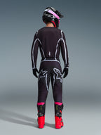Piloto de motocross visto de costas a usar o Conjunto de Equipamento Alpinestars 2026 Fluid Apex, camisola e calças pretas com linhas geométricas cinzentas e logótipos de estrela, capacete preto com detalhes cor-de-rosa, botas vermelhas e pretas vibrantes, equipamento de motocross coordenado