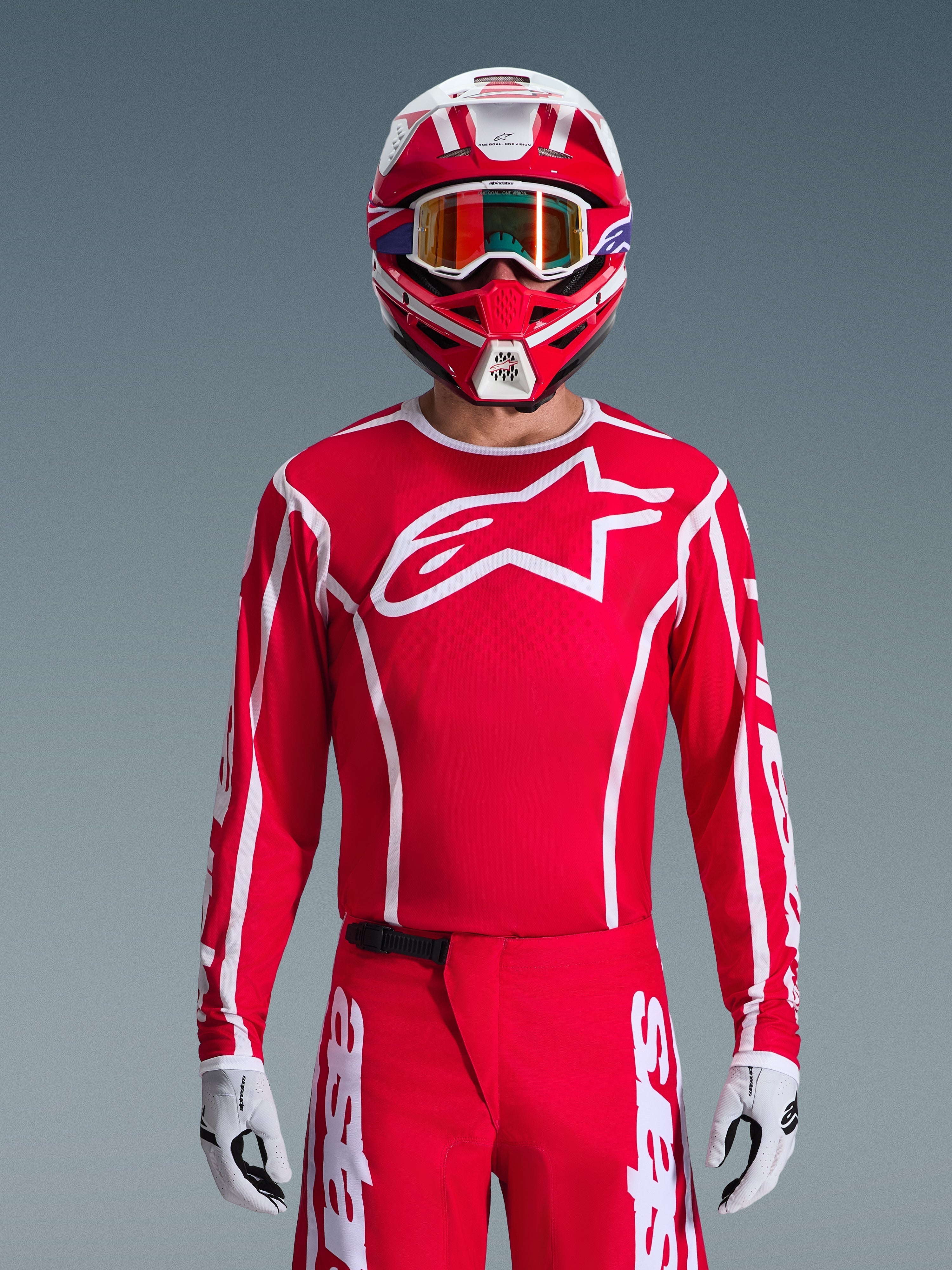 Alpinestars 2026 Fluid Apex Jersey, camisola de motocross, vermelha e branca, usada por um piloto com capacete vermelho e branco a condizer e óculos cor-de-laranja, com um logótipo branco proeminente no peito, corte atlético, parte de um conjunto de equipamento de corrida off-road coordenado