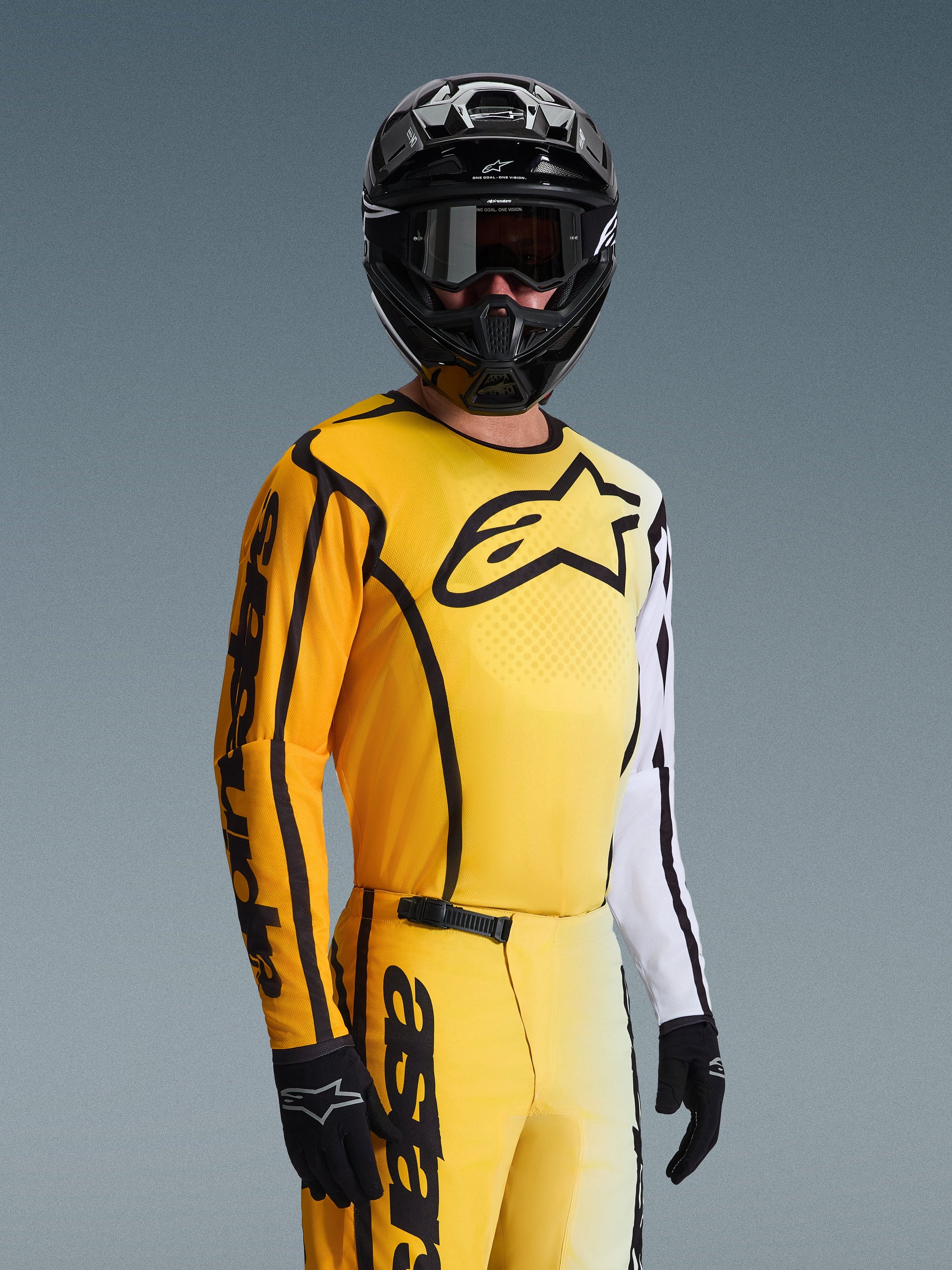 Camisola Alpinestars 2026 Fluid Apex, camisola de motocross, amarela e preta com detalhes brancos, usada por um piloto com capacete e óculos pretos, grande logótipo de estrela preto no peito, conjunto de equipamento de corrida off-road coordenado