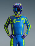 Piloto de motocross a usar a camisola Alpinestars 2026 Fluid Apex em Azul Amarelo Fluo, com uma base azul vibrante, grafismos em amarelo fluorescente e um logótipo grande no peito, combinada com capacete e luvas a condizer, concebida para corridas de motocross e todo-o-terreno