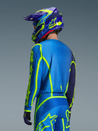 Alpinestars Camisola Fluid Apex 2026, Blue Yellow Fluo, vista traseira do piloto a usar calças de motocross e capacete a condizer, com gráficos geométricos em amarelo fluorescente e um ajuste atlético relaxado, equipamento de corrida off-road coordenado