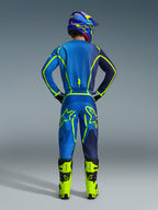Piloto de motocross visto de costas com equipamento de corrida completo, apresentando a camisola e as calças Alpinestars 2026 Fluid Apex em Blue Yellow Fluo, com detalhes em néon vibrante e logótipos destacados, botas amarelas brilhantes e capacete a condizer.