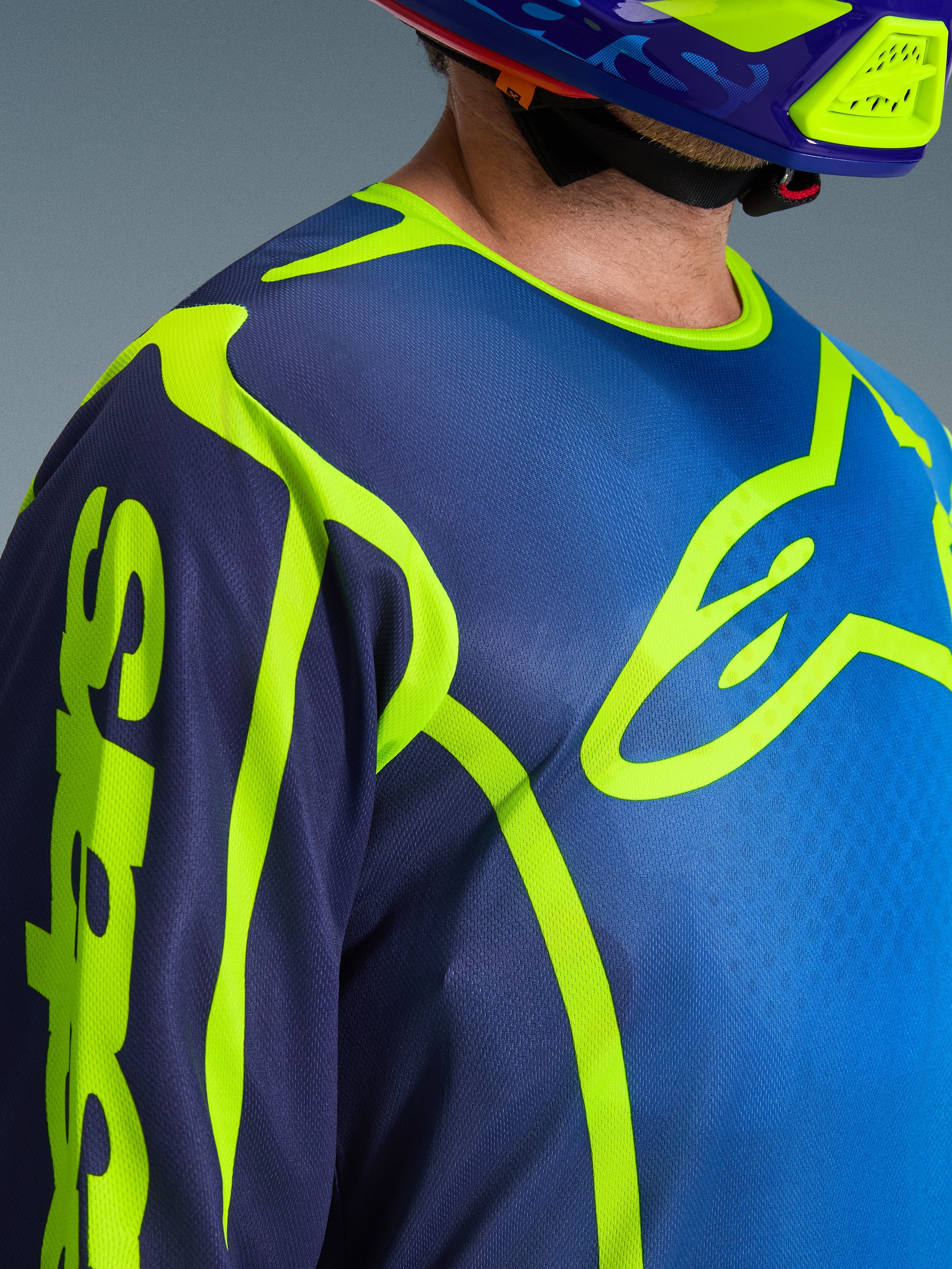 Alpinestars 2026 Fluid Apex Jersey, camisola de motocross em azul e amarelo fluo, vista aproximada mostrando o grande logótipo no peito em amarelo néon e a marca na manga, construção em polifabric respirável com gola desportiva ergonómica