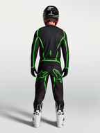 Alpinestars Fluid Apex V2, calças de motocross pretas e verdes fluorescentes, vista traseira com botas brancas.