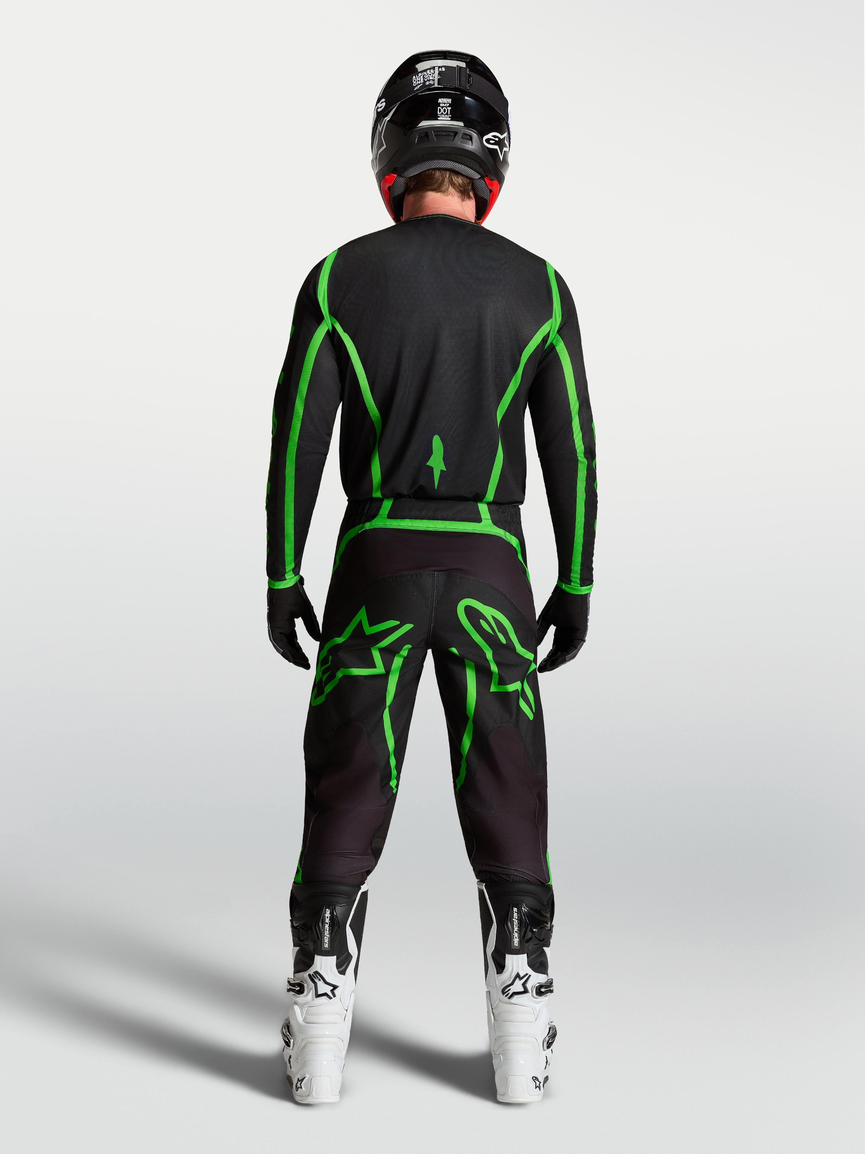 Alpinestars Fluid Apex V2, calças de motocross pretas e verdes fluorescentes, vista traseira com botas brancas.