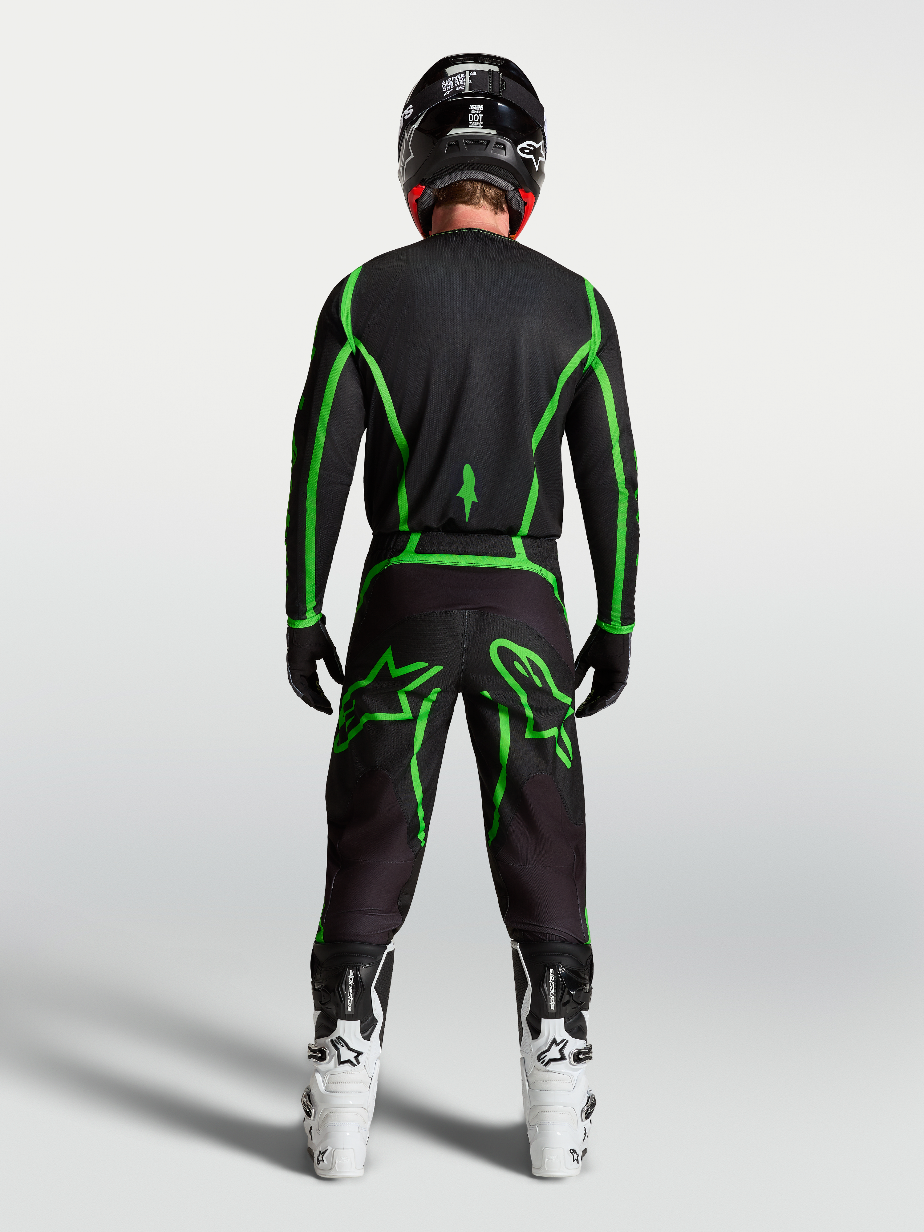 Alpinestars camisola Fluid Apex V2 para homem, em preto e verde fluorescente, vista traseira no piloto com botas brancas.