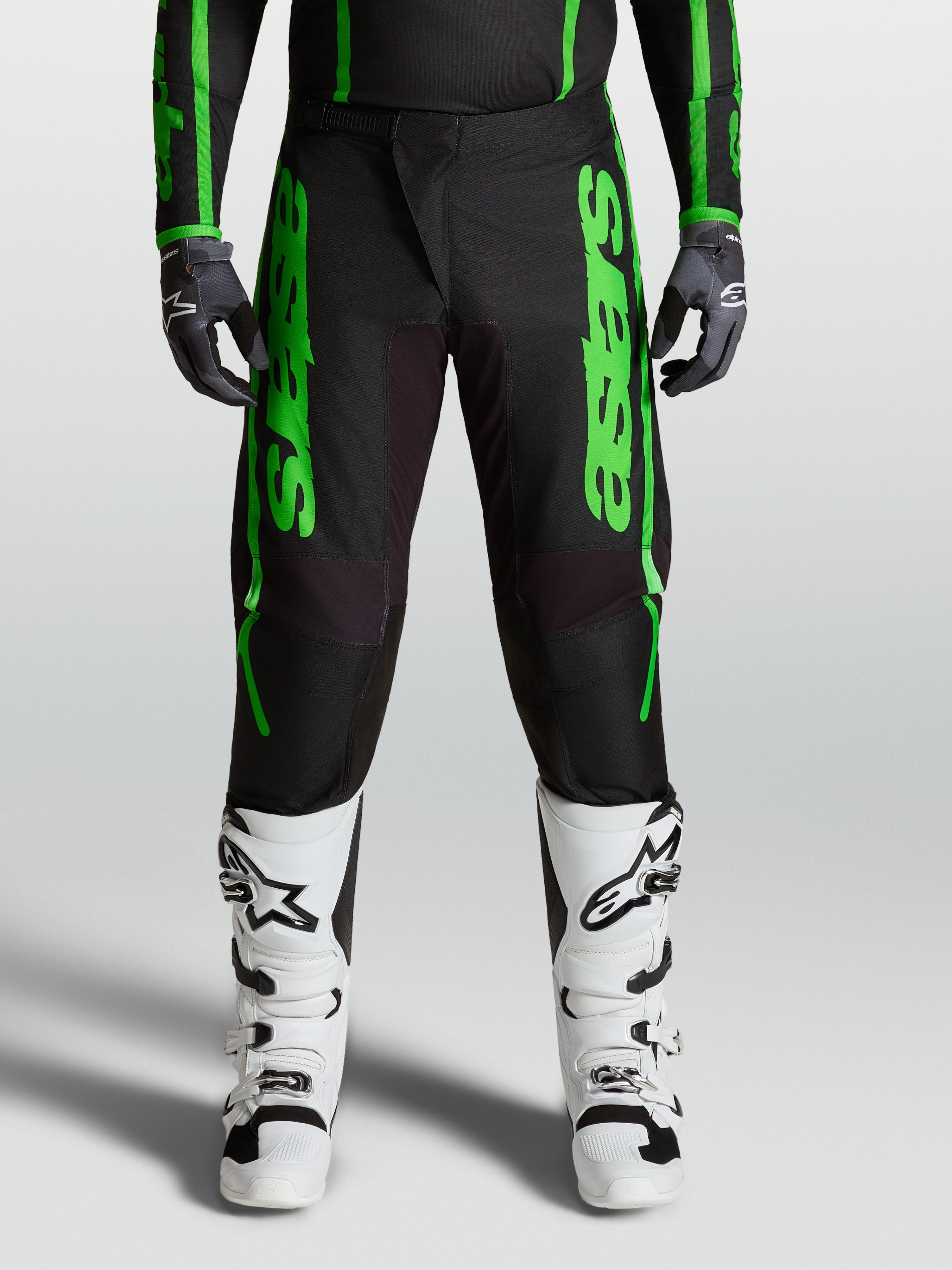 Calças Alpinestars Fluid Apex V2, calças de motocross para homem, verdes e pretas, com joelhos reforçados e botas brancas.