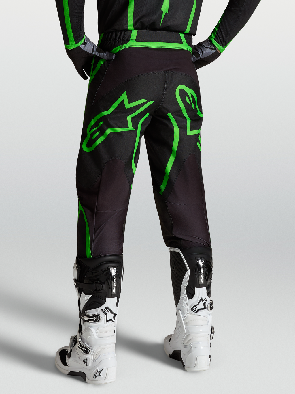 Alpinestars Fluid Apex V2, calças de motocross para homem, pretas e verdes fluo, vista traseira no modelo com botas brancas.