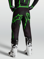 Alpinestars Fluid Apex V2, calças de motocross para homem, pretas e verdes fluo, vista traseira no modelo com botas brancas.