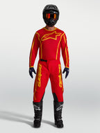 Alpinestars camisola Fluid Apex V2 e conjunto Fluid Apex V2, equipamento de motocross em vermelho e dourado num modelo.