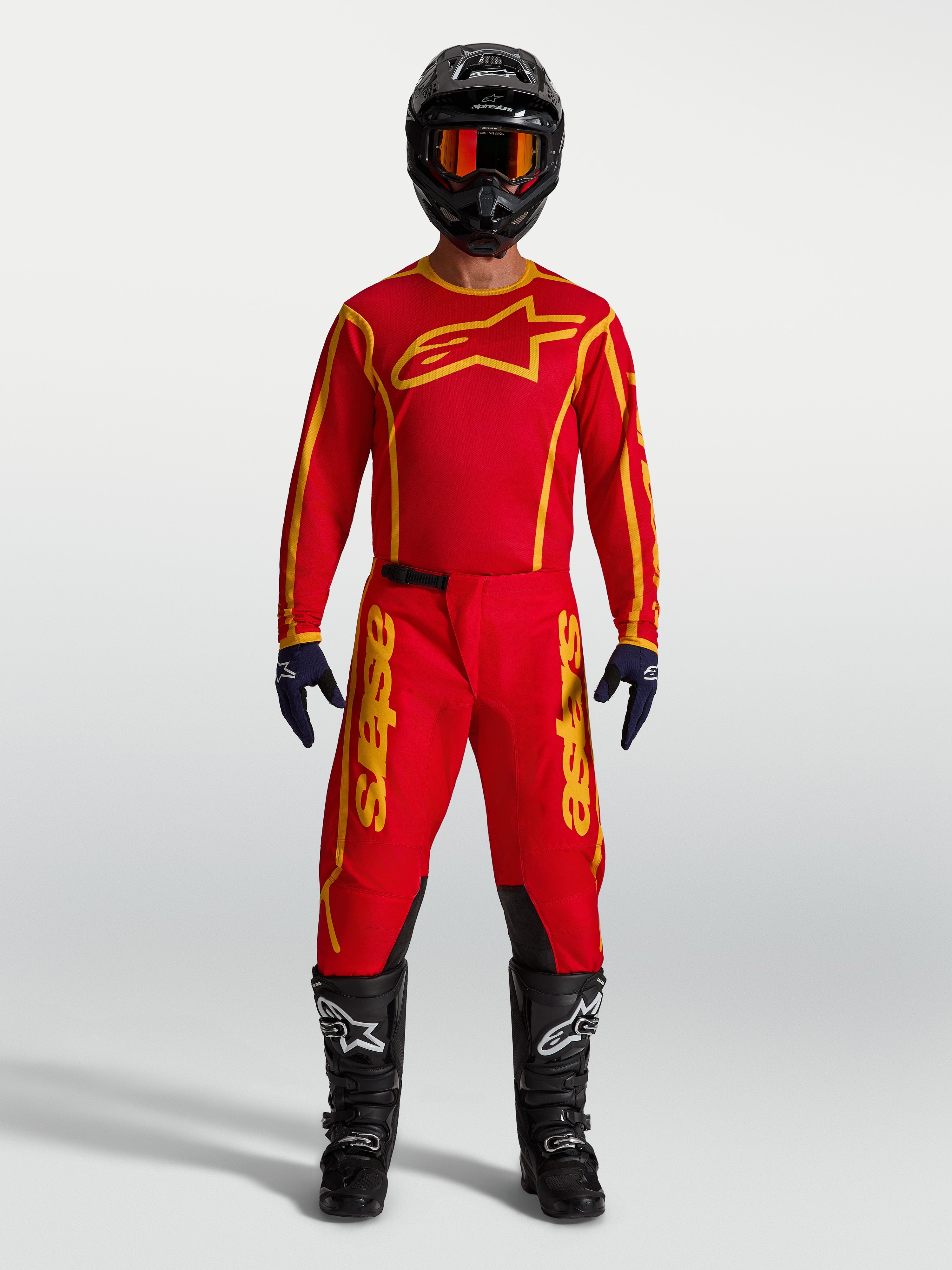 Alpinestars camisola Fluid Apex V2 e conjunto Fluid Apex V2, equipamento de motocross em vermelho e dourado num modelo.