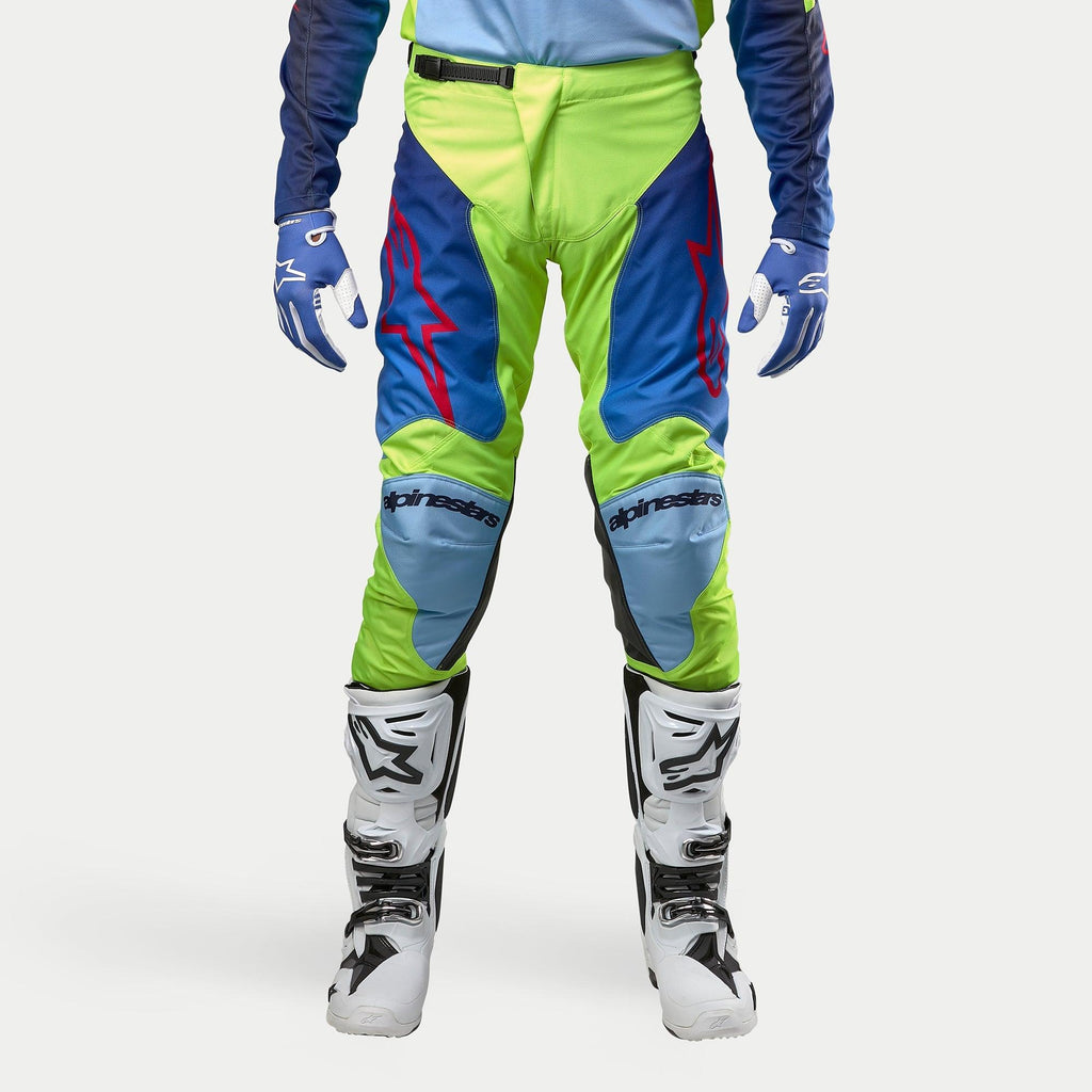 Alpinestars 2024 Racer Hoen Pants, Motocross Pants, Yellow Fluo and Blue Night Navy, worn with white and black motocross boots and blue gloves, featuring bold red logos, light blue knee panels, and a sporty ergonomic design for off-road riding