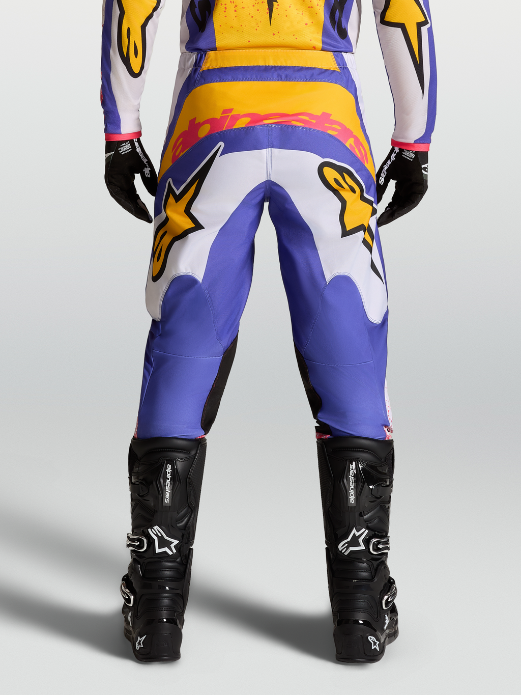 Alpinestars Calças Fluid Drag, calças de motocross em azul e dourado, vista traseira, assento reforçado e botas pretas.