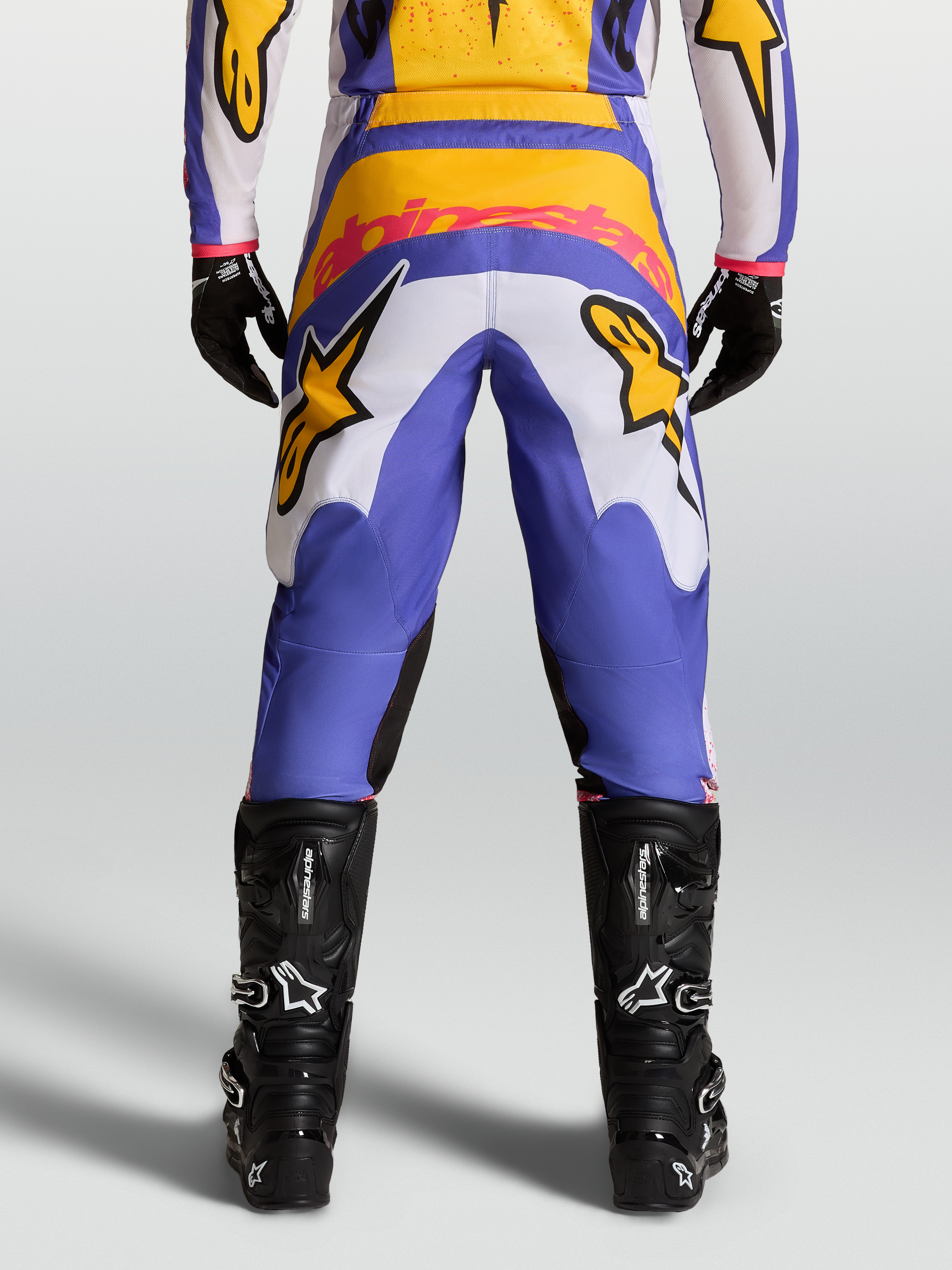 Alpinestars Calças Fluid Drag, calças de motocross em azul e dourado, vista traseira, assento reforçado e botas pretas.