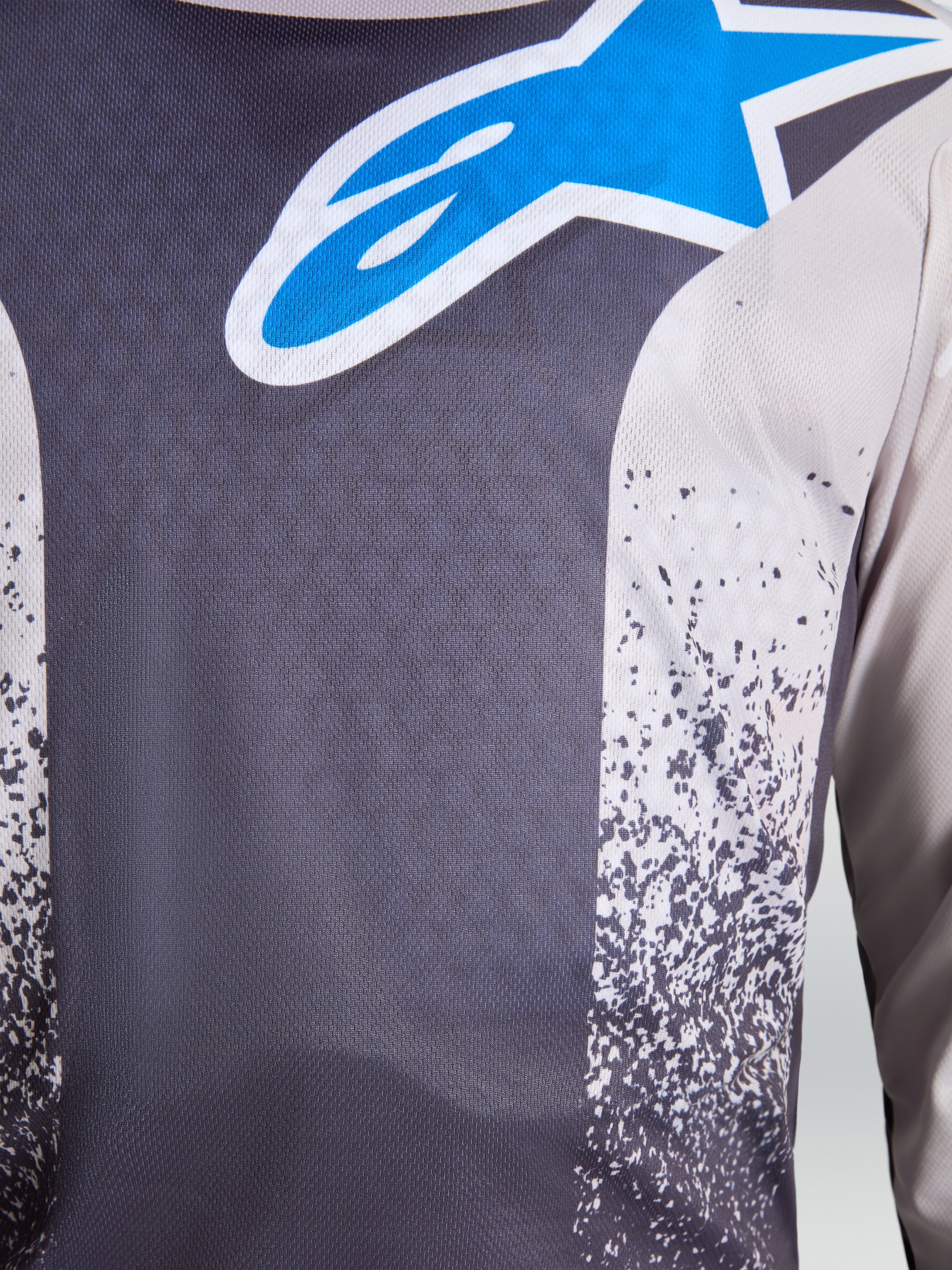 Alpinestars Camisola Fluid Drag, camisola de motocross masculina, cinzenta e azul, pormenor do logótipo Astars e tecido respirável.