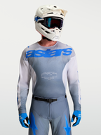 Alpinestars Camisola Racer Amber, camisola de motocross para homem, cinzenta e azul, com capacete de MX branco e óculos