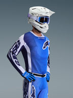 Alpinestars 2026 Racer Air Portl Jersey, camisola de motocross, azul Ucla e branco, usada com capacete branco, óculos azuis e luvas a condizer, com um design de malha respirável para corridas de motocross a altas temperaturas