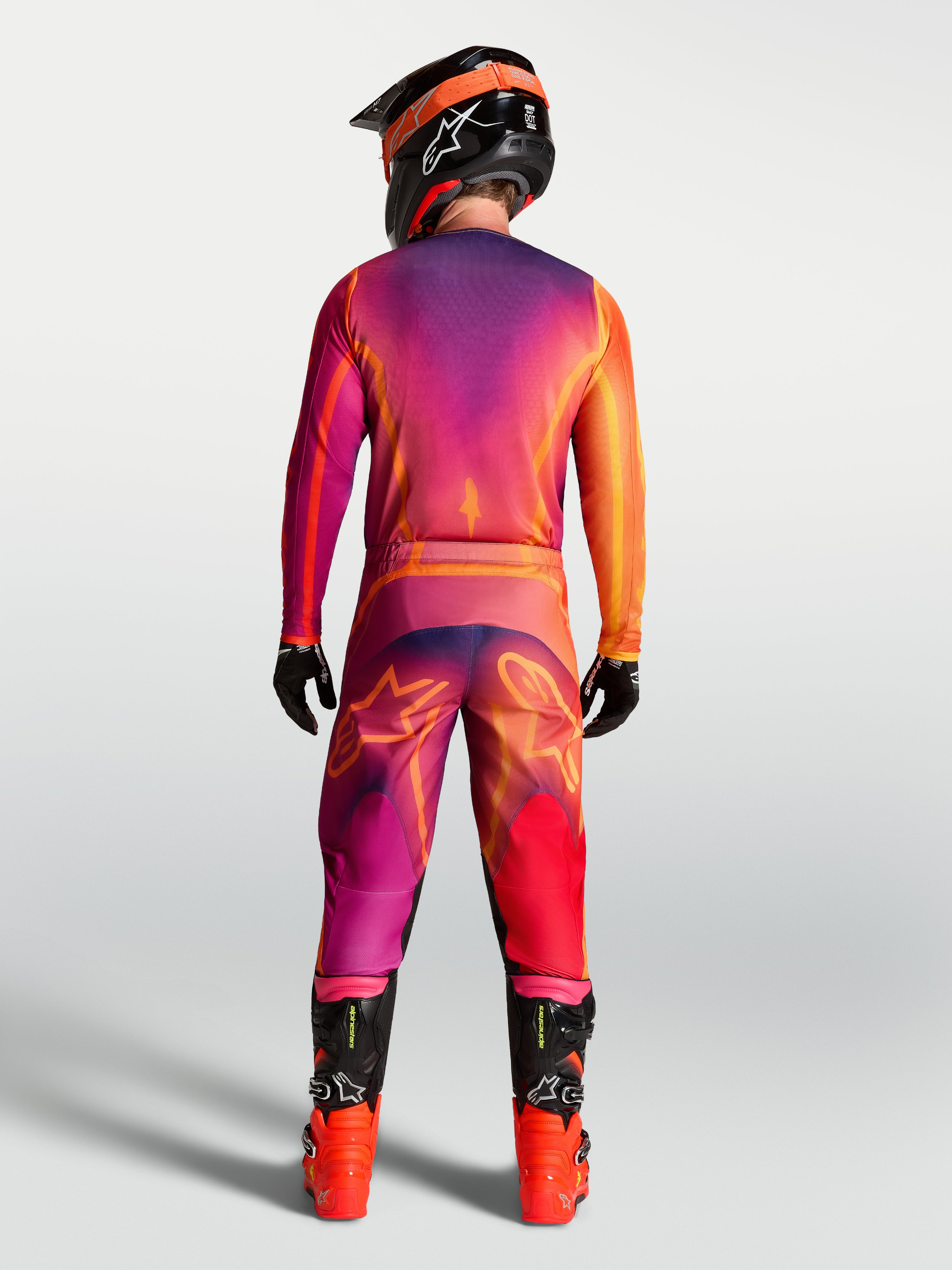 Alpinestars Camisola Fluid Kepler, camisola de motocross para homem, roxa e laranja, vista traseira do piloto com calças e equipamento de todo-o-terreno a condizer.