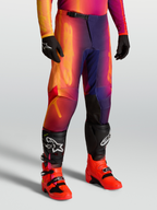Alpinestars Calças Fluid Kepler, calças de motocross todo-o-terreno roxas e cor de laranja, ajuste desportivo com joelhos reforçados, usadas com botas e luvas pretas.