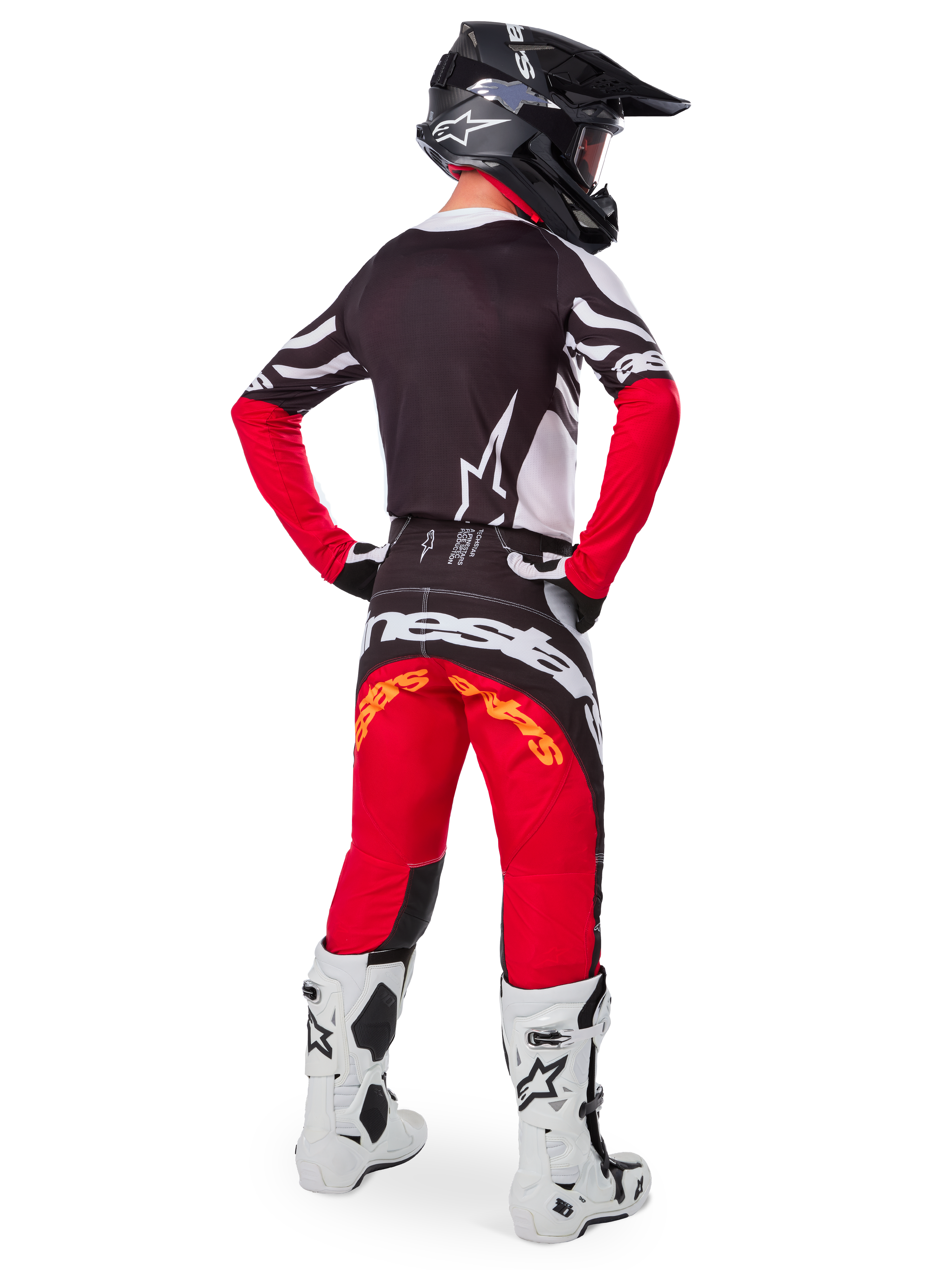 Rear view of a motocross rider wearing the Limited Edition Techstar Deep Gear Set, featuring a black jersey with white and red accents, matching red and black pants with 'Alpinestars' branding, white racing boots, and a black helmet, showcasing the complete off-road racing outfit.